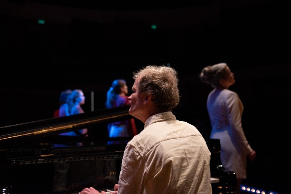 Bert van den Brink achter de piano met erachter Wishful Singing