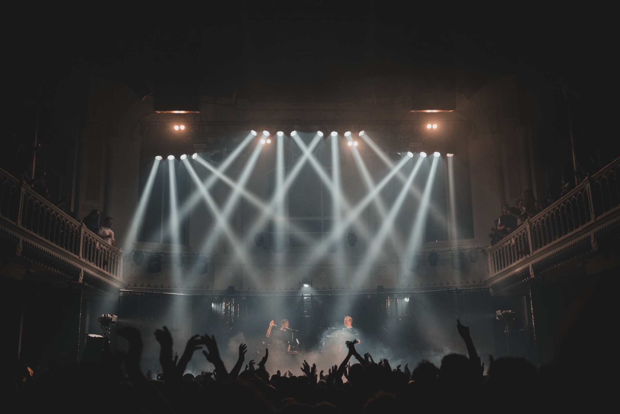Een foto van achterin de zaal van Paradiso. De spots richten van bovenin de zaal op het podium.