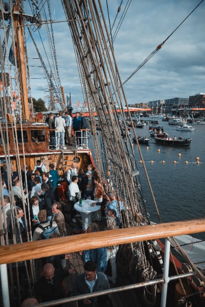 De borrel van DVME op de Bark Europa tijdens SAIL Amsterdam, met daarachter bootjes die langsvaren