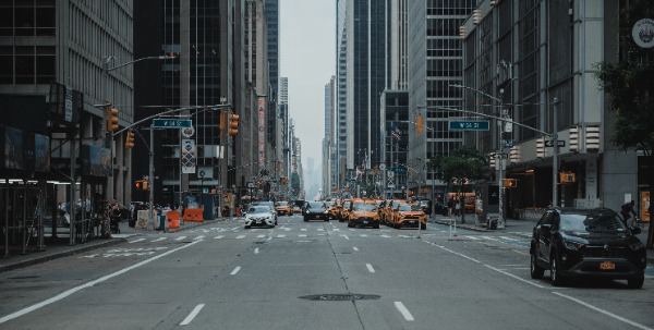 Een drukke straat in New York. We kijken de diepte in langs wolkenkrabbers, auto's en taxi's.