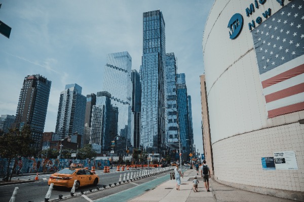Wolkenkrabbers en een gele taxi in New York, langs een gebouw met een Amerikaanse vlag.