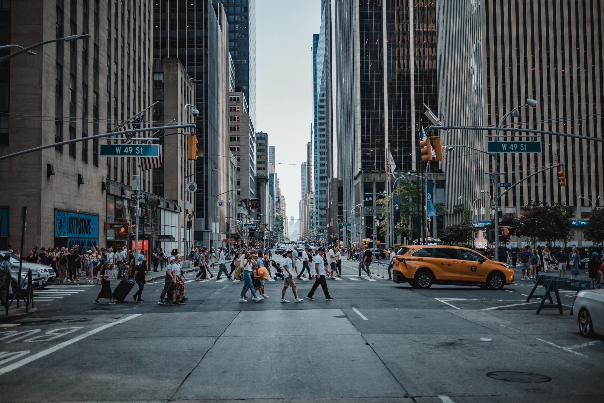 Een drukke straat in New York. We kijken de diepte in langs een aantal auto's en veel voetgangers