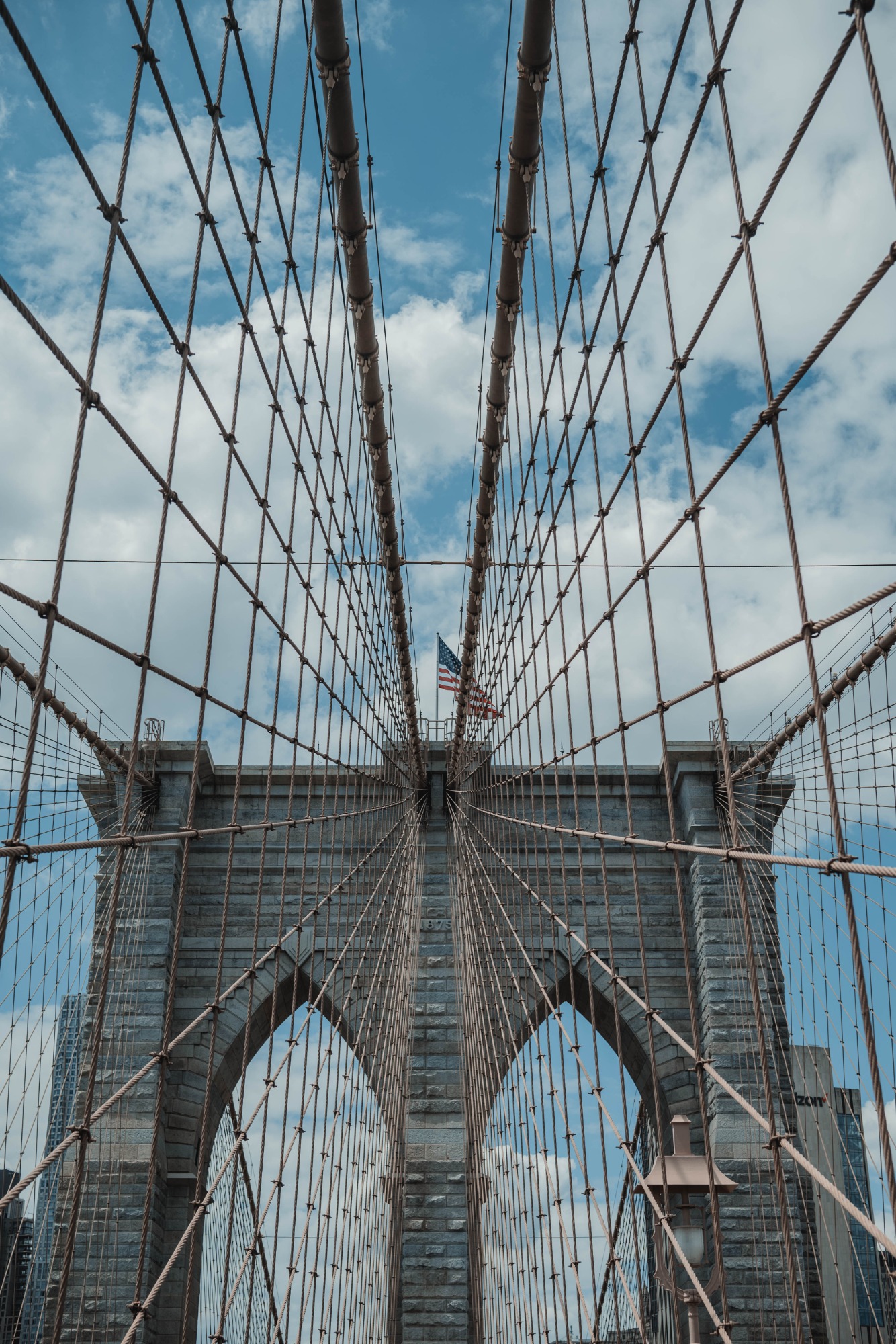 De kabels van de Brooklyn Bridge, met een wapperende Amerikaanse vlag aan het einde.