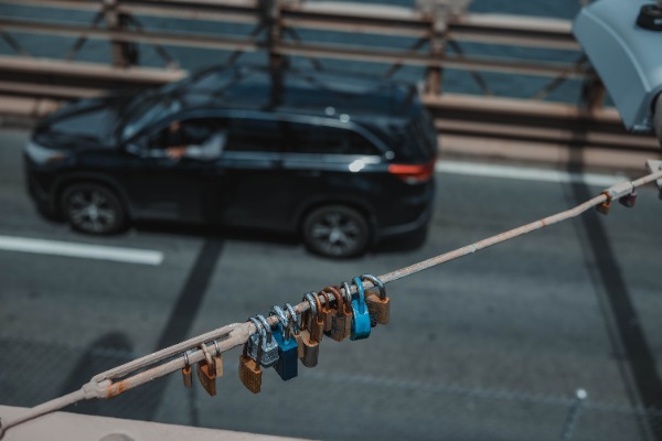 Een auto rijdt over de Brooklyn Bridge en we zien slotjes hangen aan een kabel.