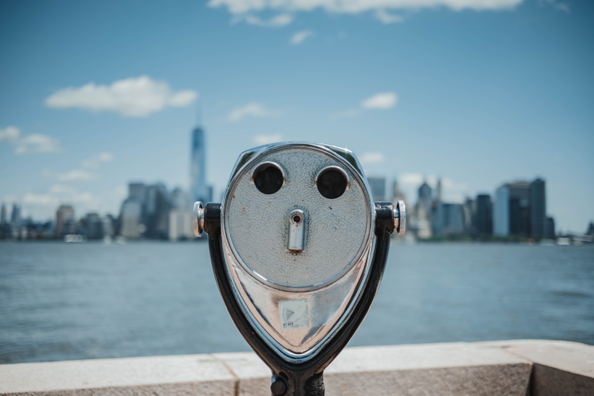 Een verrekijker op Ellis Island, met de skyline van New York erachter.