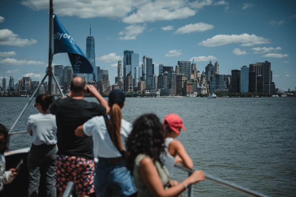 Een groepje toeristen staat voorop een boot en maakt een foto van de skyline van New York.