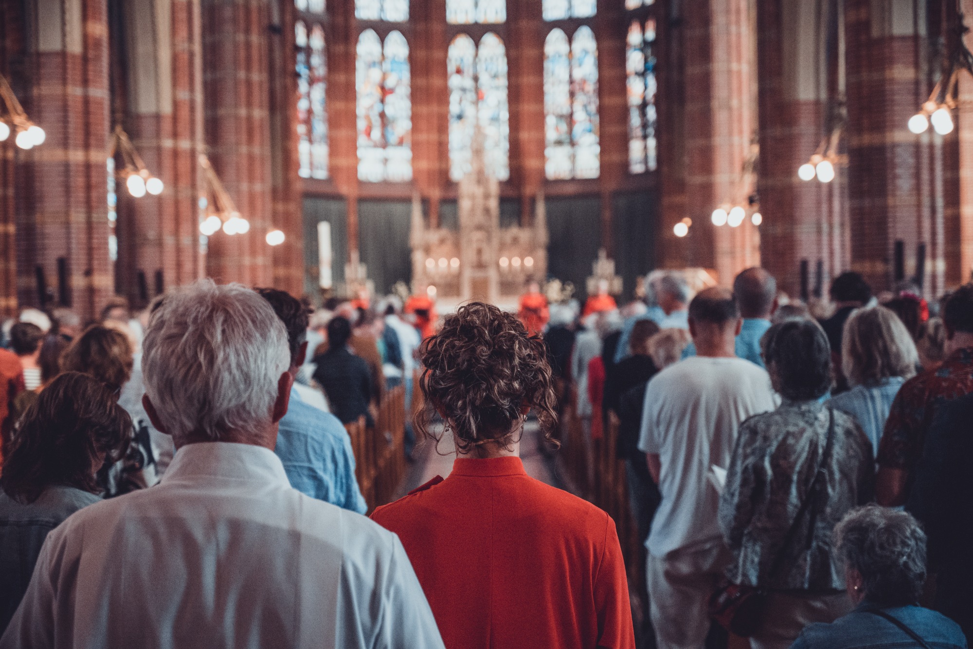 Herman Finkers en de zangeressen van Wishful Singing van achteren gefotografeerd. Ze lopen naar voren door een volle kerk.