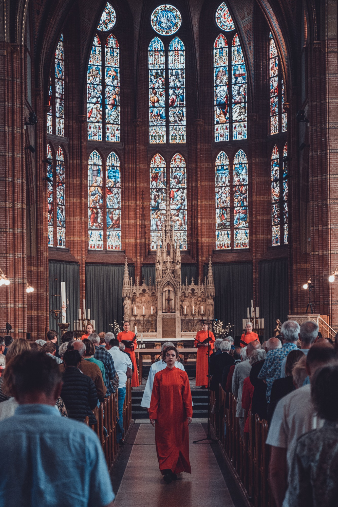 Herman Finkers en de zangeressen van Wishful Singing gefotografeerd. Ze lopen naar achteren door een volle kerk.