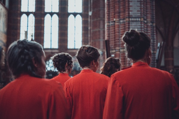 De zangeressen van Wishful Singing van achteren gefotografeerd. Ze kijken allemaal naar rechts.